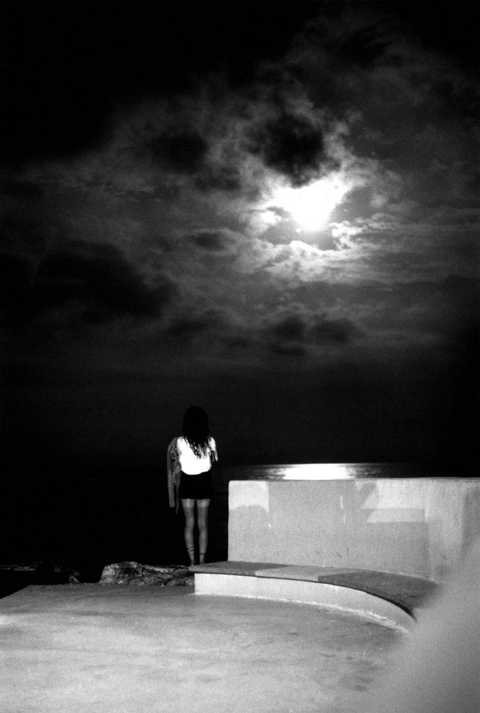 Una giovane donna di notte osserva la luna attraverso le nubi